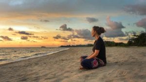 Woman sits and meditates on the beach at sunrise